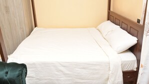 Una cama individual con cabecera de madera y cubrecama blanco sencillo.