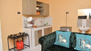 Cocina compacta con estufa a gas, una mesita y un sofá decorado con cojines.