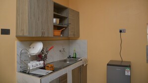 Una cocina con armarios de madera, un lavaplatos, un escurreplatos y un refrigerador pequeño.