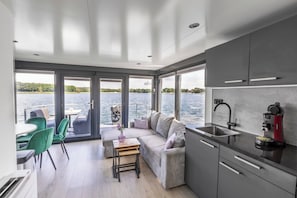 A modern interior with a kitchen, dining area, and large windows overlooking a body of water.