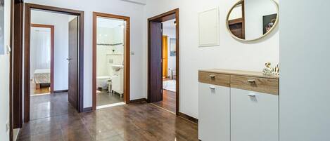 Un pasillo con piso de madera que conduce a un baño con inodoro y lavamanos. Hay puertas a ambos lados del pasillo.