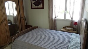 Une chambre à coucher avec un lit, une armoire en bois, un miroir, une table de chevet avec une lampe et un tableau encadré accroché au mur.