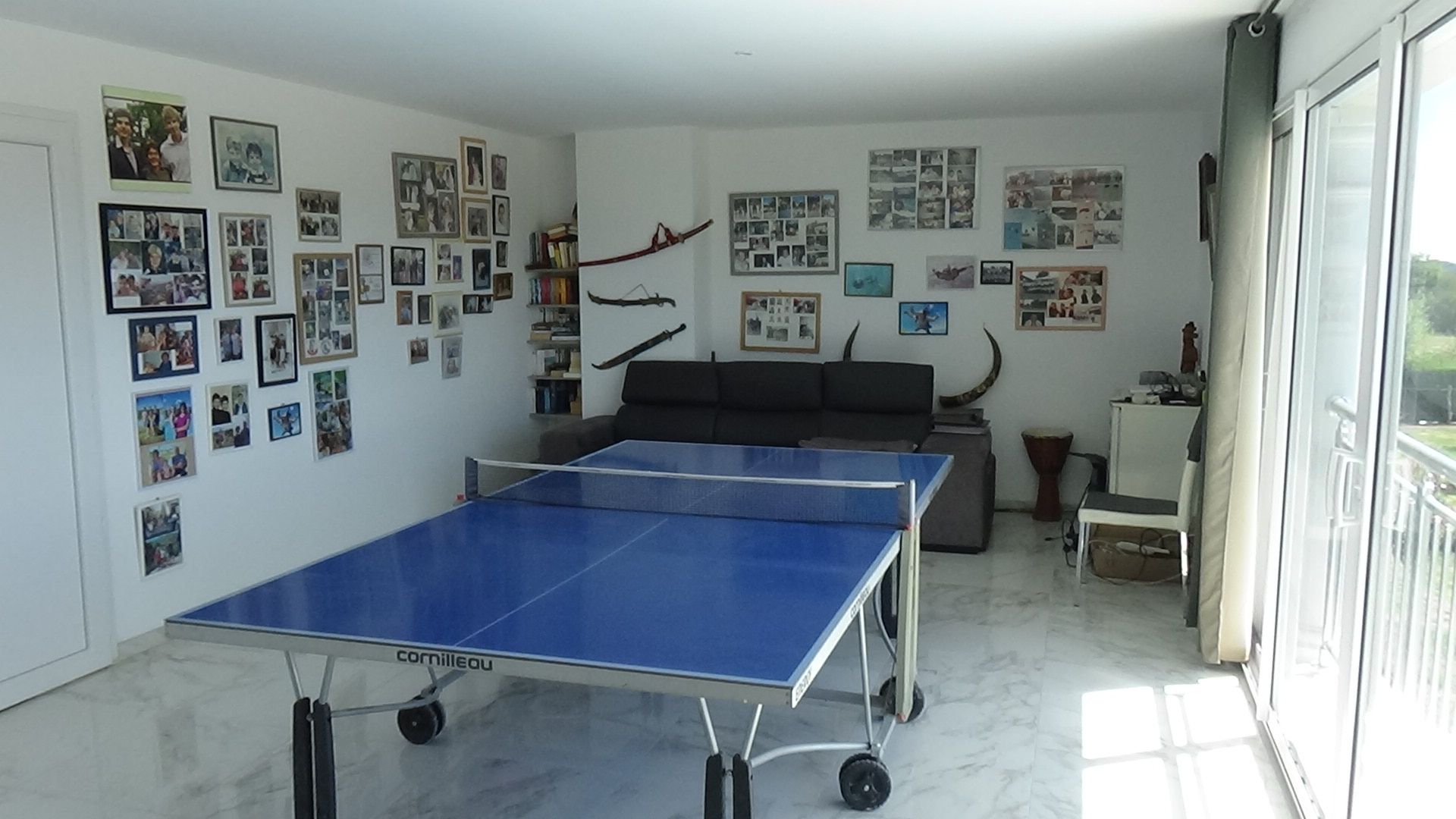 A room with a ping pong table, a sofa, and a wall covered with photos.