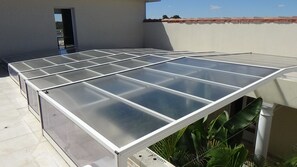 A rooftop with a glass-enclosed patio area, surrounded by plants and a building with a red-tiled roof. - Unique house with an interior garden and a view of the Pyrenees mountain range (Toujouse)