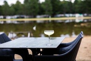 A table with a glass of drink, chairs, and a view of a body of water with reflections.