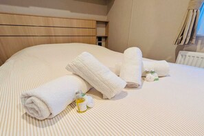 A neatly made bed with rolled white towels and two small bottles of toiletries. - Mobile Home with Shared Pool for 6 Guests (Zonhoven)