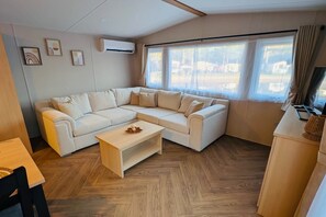 A modern living room with a sectional sofa, a wooden coffee table, and a TV on a stand. - Mobile Home with Shared Pool for 6 Guests (Zonhoven)