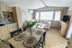 A modern, well-lit living area with a sofa, a dining table with placemats, and a television on a cabinet.