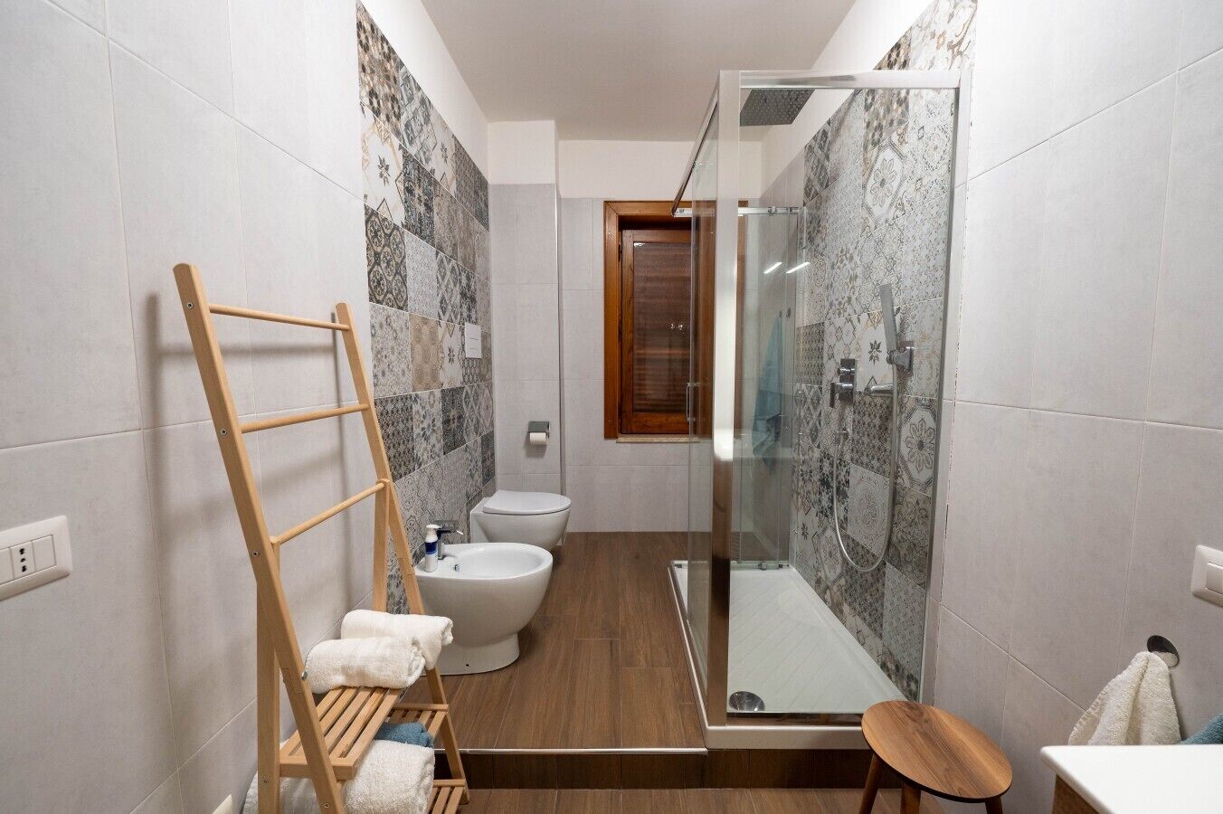 A bathroom with a shower, toilet, and bidet. There is a wooden ladder and a towel rack.