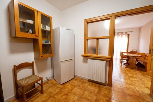 A compact kitchen with a refrigerator, wooden cabinets, a chair, and a window.