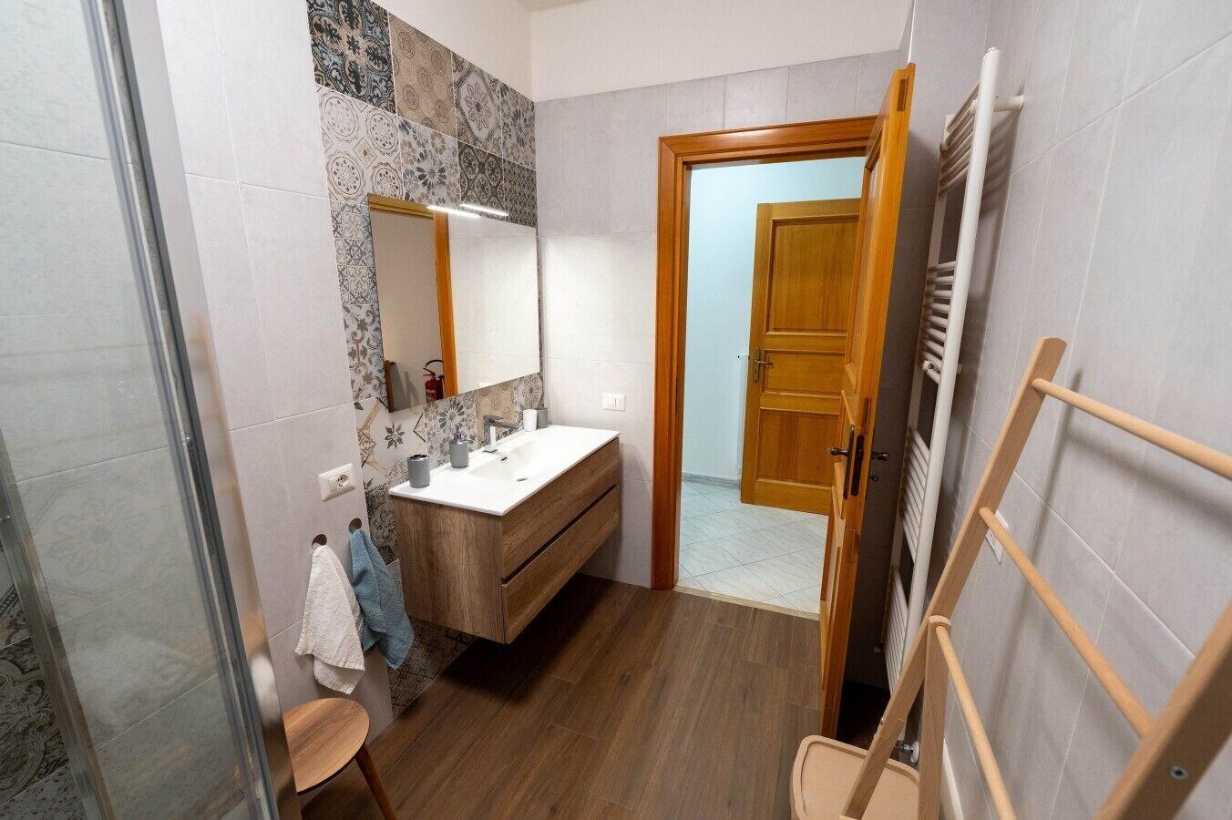 Een badkamer met een houten wastafelmeubel, een spiegel, een douche en een handdoekhouder.