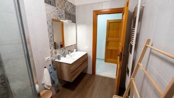 Een badkamer met een houten wastafelmeubel, een spiegel, een douche en een handdoekhouder.