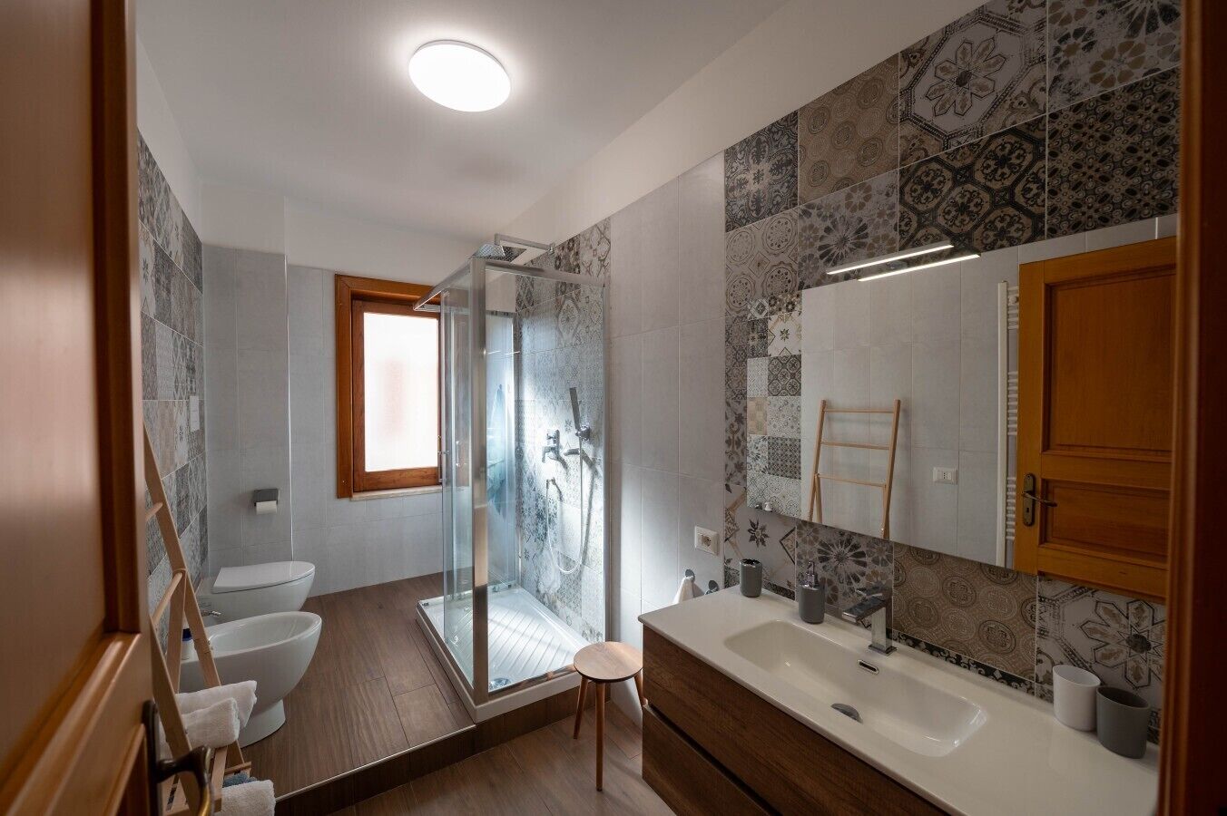 Ein modernes Badezimmer mit einer gläsernen Duschkabine, einem Holzbadezimmer-Möbel und gefliesten Wänden.
