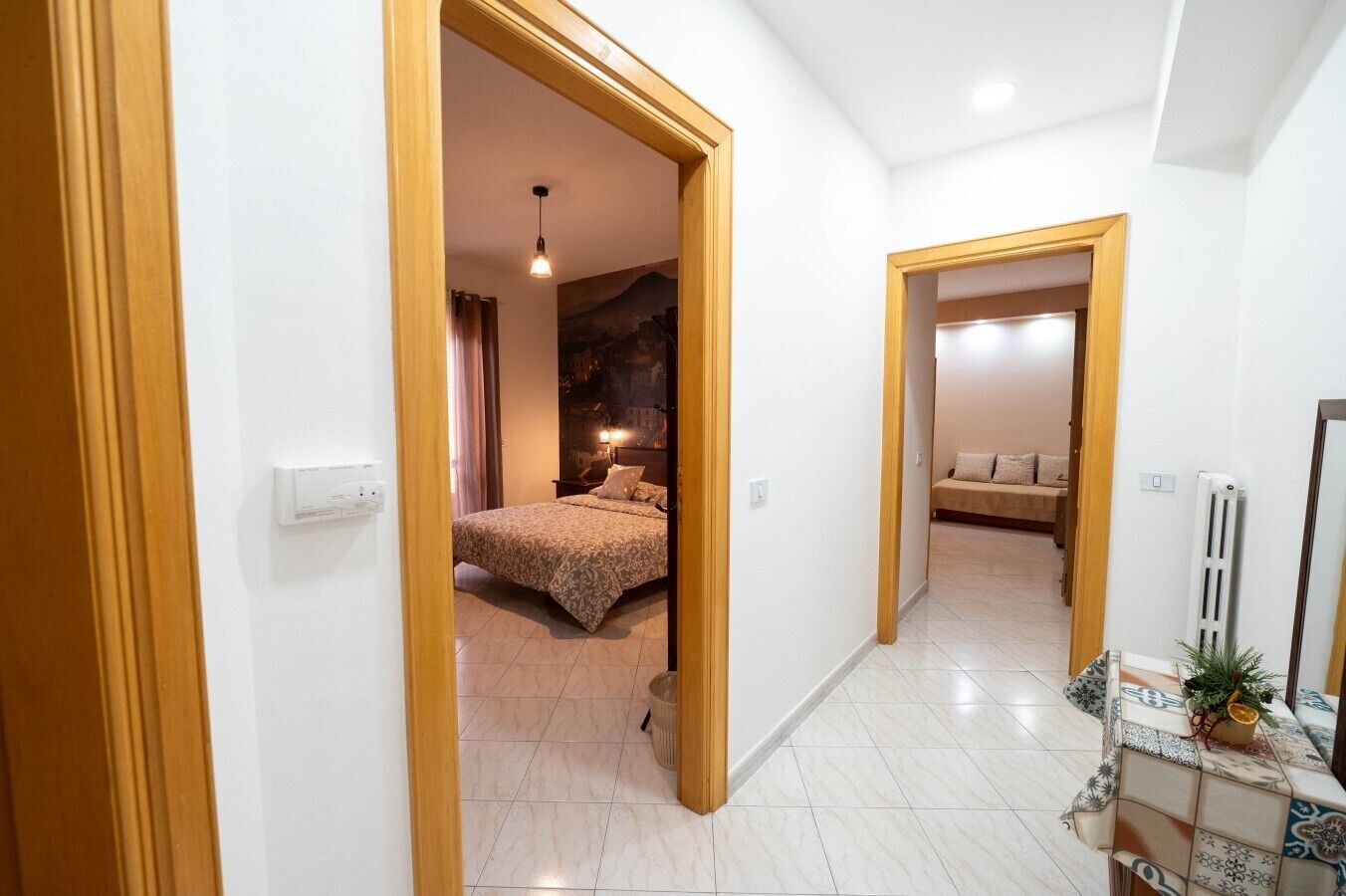 Un pasillo que conduce a un dormitorio con una cama, una mesita de noche y una lámpara de pared.