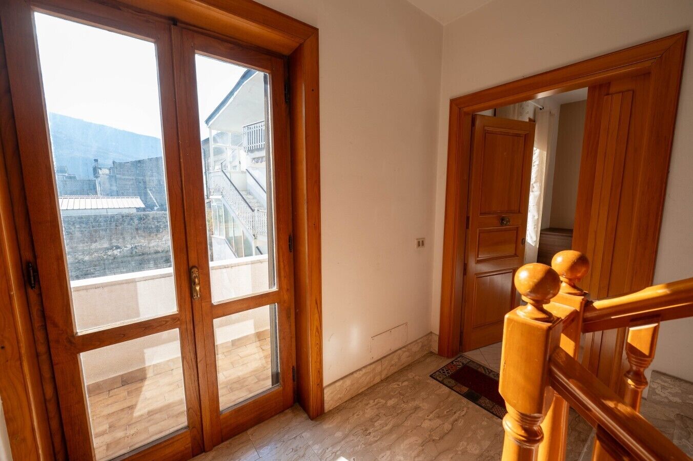 Una habitación con puerta de madera que da a un balcón, una escalera de madera y vista a un edificio con balcón.