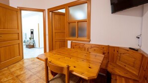 A dining area with a wooden table and chairs, a TV mounted on the wall, and a door leading to another room.
