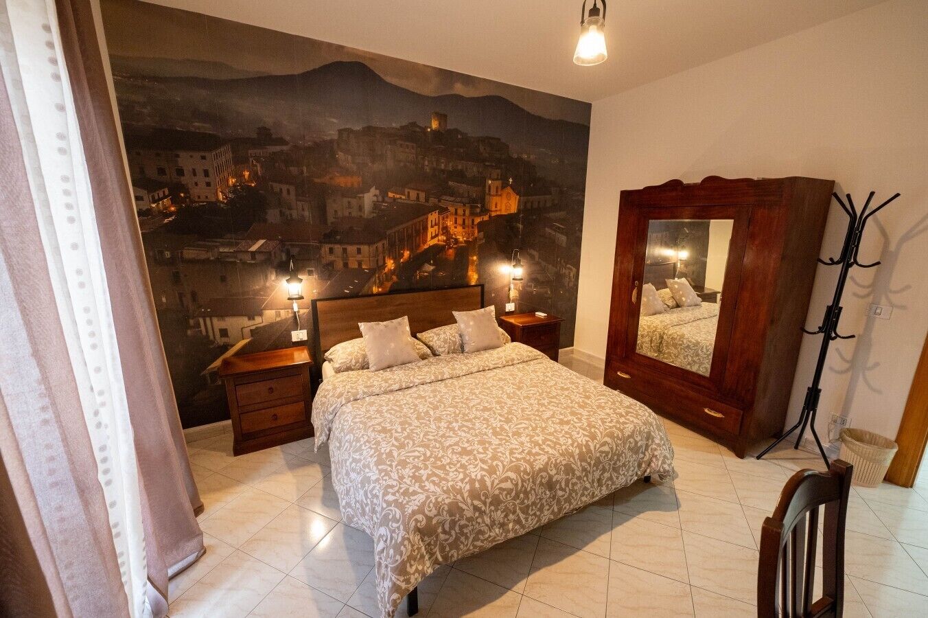 A bedroom with a large bed, a nightstand, a dresser, a mirror, and a cityscape painting on the wall.