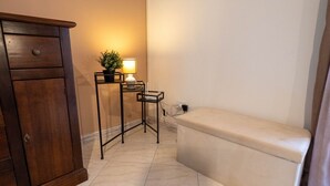A bathroom with a wooden cabinet, a small table with a lamp, and a bench.