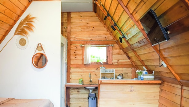 Interior de una cabaña con habitación en el altillo, una pequeña kitchenette y ventana con vistas.