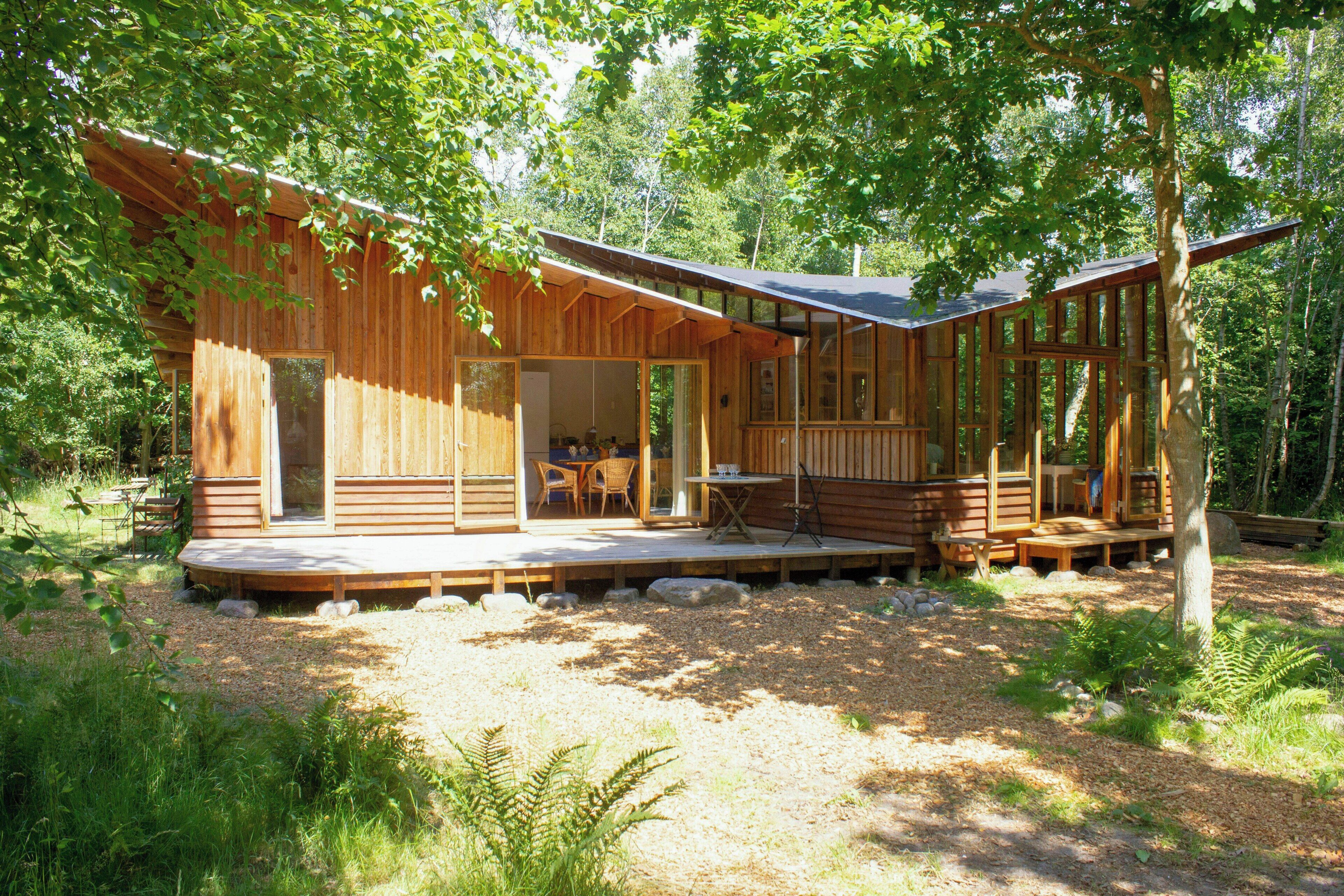 Una baita di legno con veranda, ampie finestre e zona pranzo.