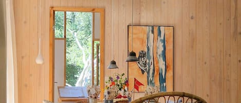 A dining area with a wooden table, wicker chairs, and a painting on the wall.