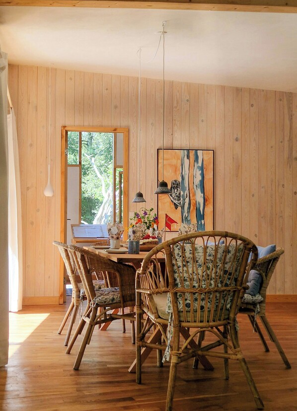 A dining area with a wooden table, wicker chairs, and a painting on the wall.