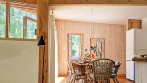 A wooden interior with a dining area, wooden beams, and a view through the windows. - Hand-built timber and clay cottage by Bøtøskoven (Gedser)