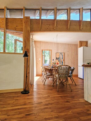 A wooden interior with a dining area, wooden beams, and a view through the windows. - Hand-built timber and clay cottage by Bøtøskoven (Gedser)