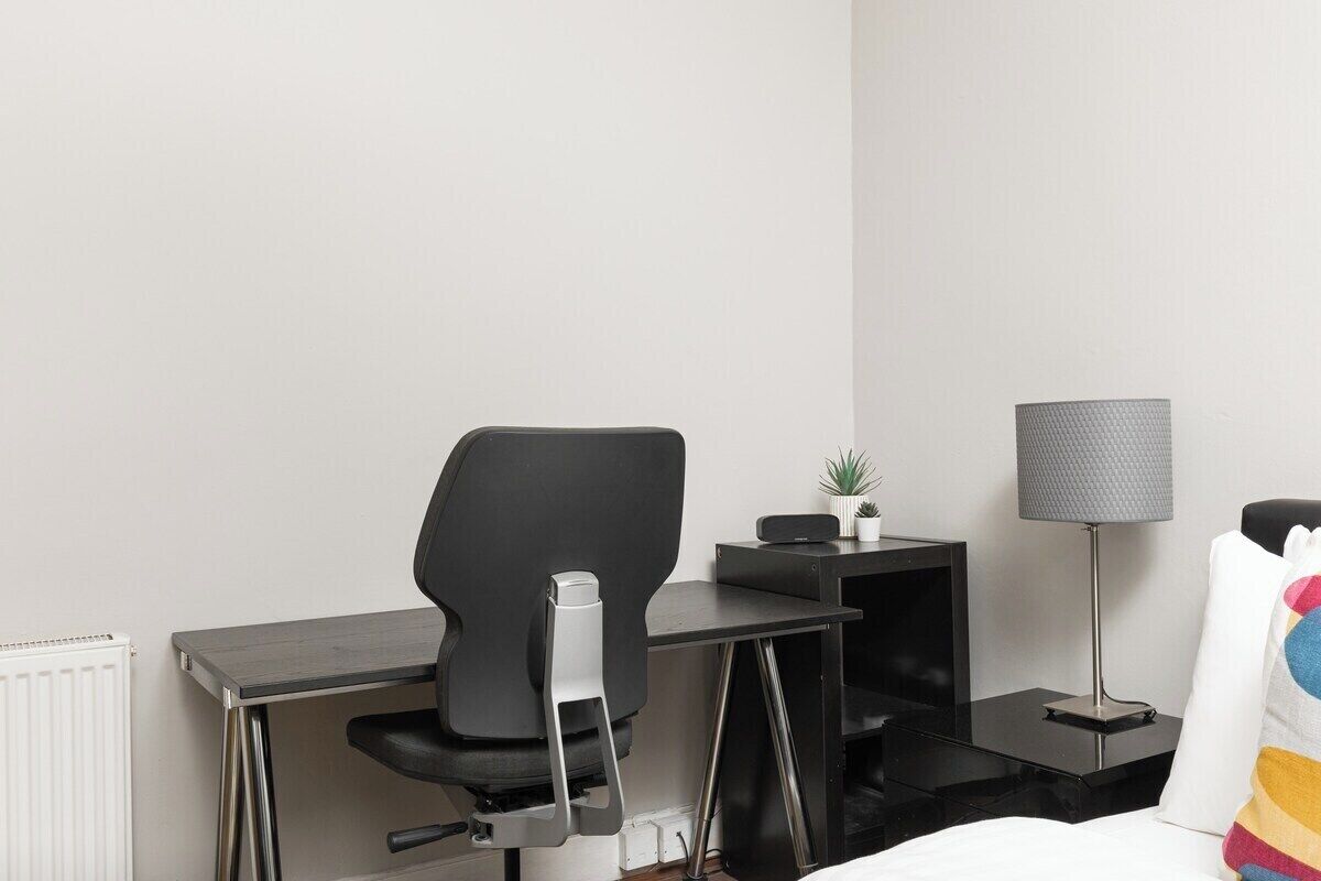 Una habitación de hotel con escritorio, silla, lámpara y una cama con almohada colorida.