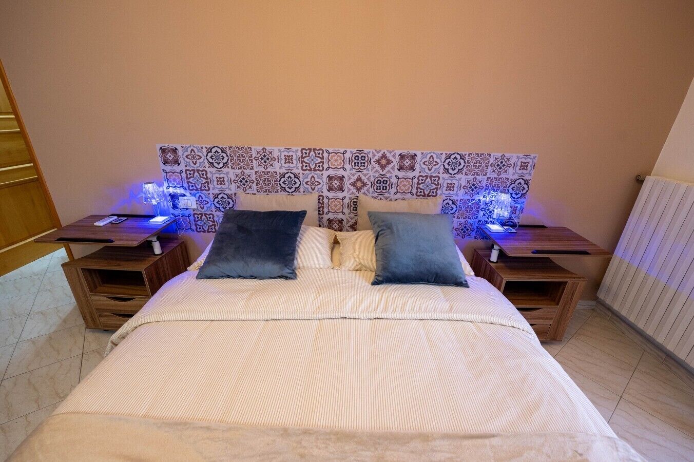 Une chambre d’hôtel avec un lit, deux tables de chevet, une tête de lit à motifs et un radiateur.