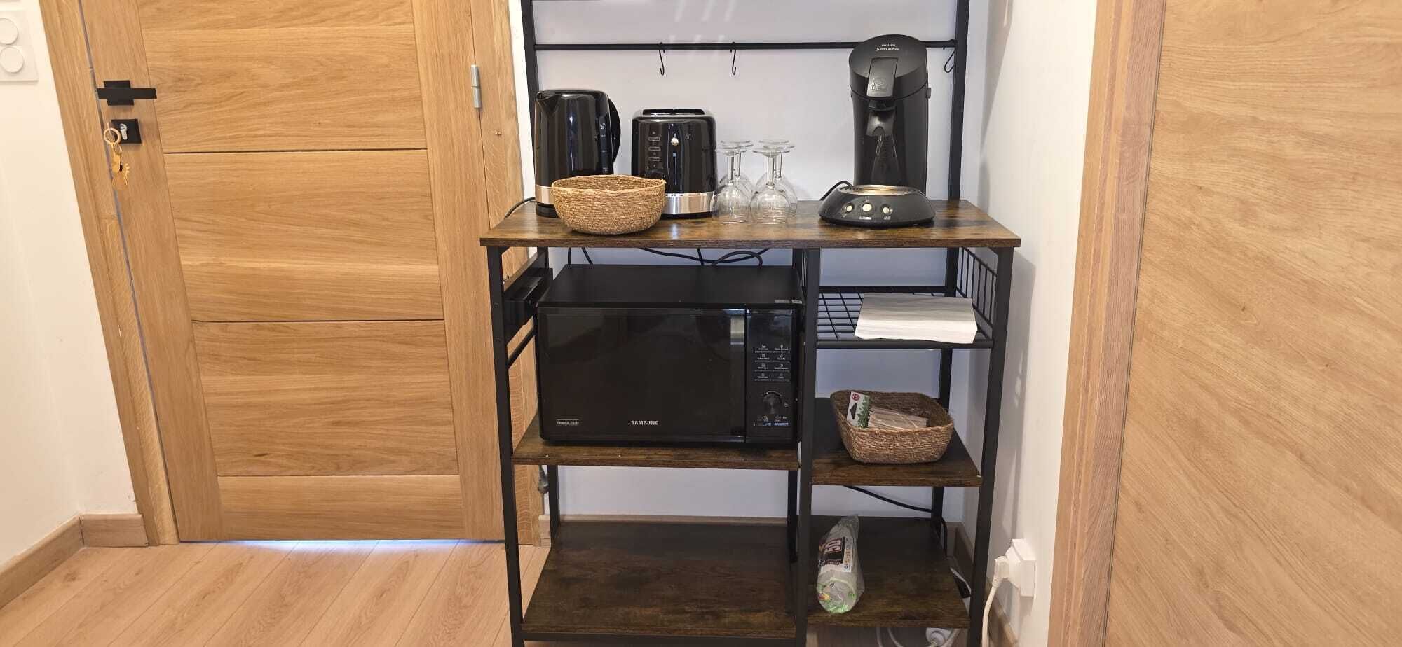 Cocina compacta con microondas, tostadora y cafetera sobre un estante de madera.