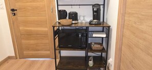 Cocina compacta con microondas, tostadora y cafetera sobre un estante de madera.