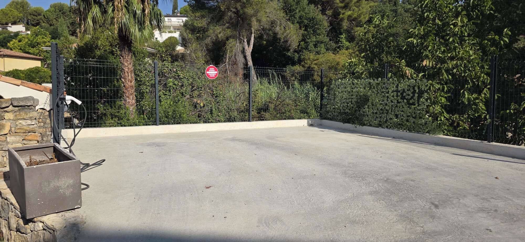 Un área pavimentada con una valla metálica y una señal de stop roja al fondo.