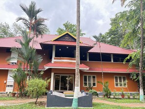 A two-story building with a red-tiled roof, surrounded by greenery and palm trees.