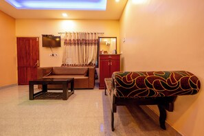 A living room with a sofa, a coffee table, a TV mounted on the wall, a cabinet, and a patterned bench. - River Country (Nedumangad)