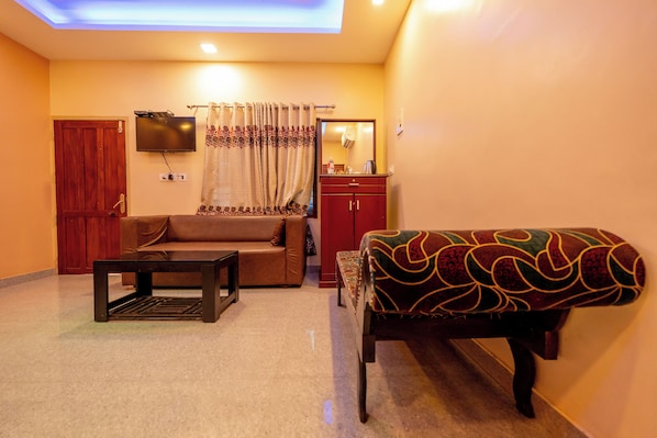 A living room with a sofa, a coffee table, a TV mounted on the wall, a cabinet, and a patterned bench.