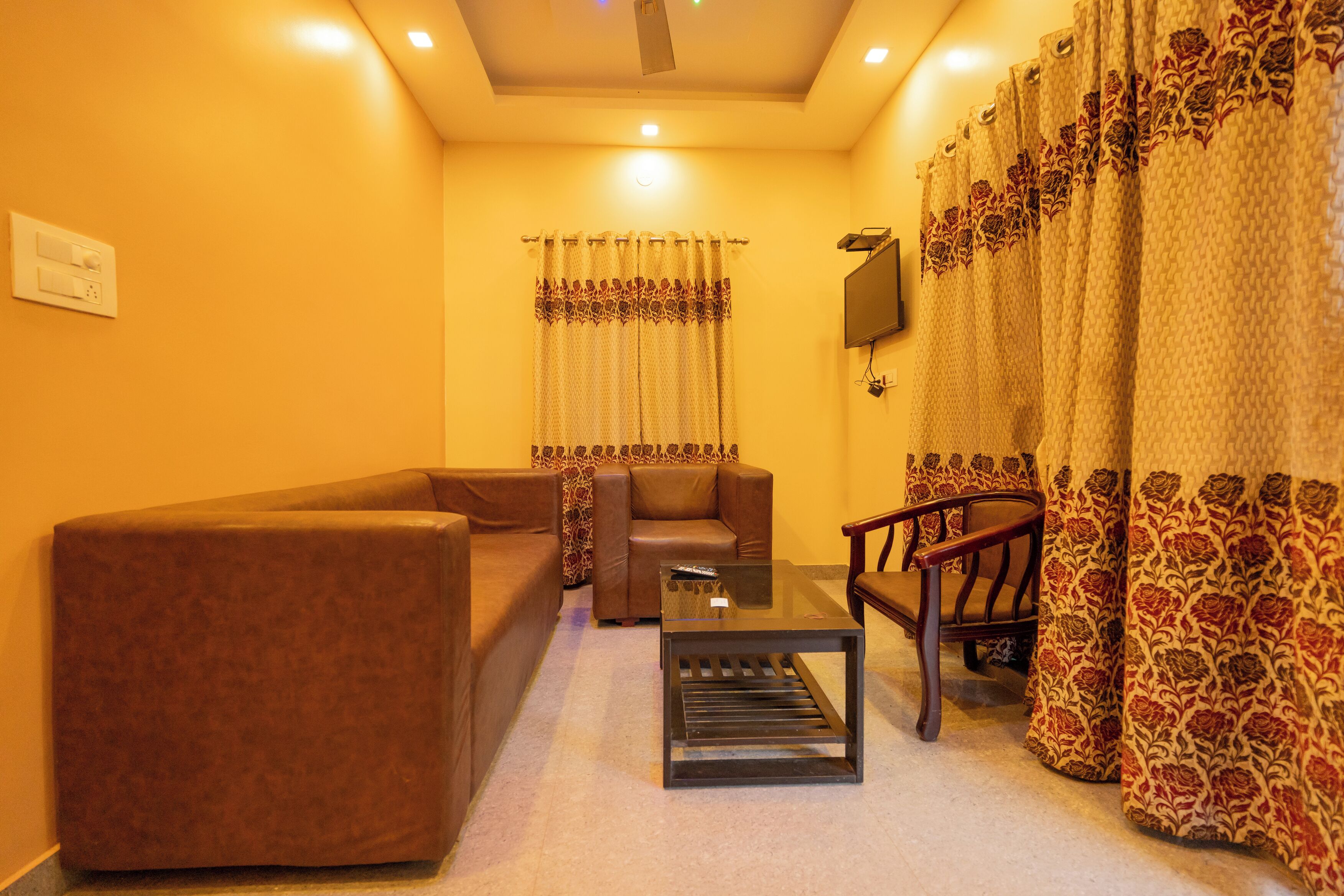 A living room with a brown sofa, a glass coffee table, and a wooden chair.