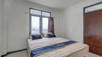 Una habitación de hotel con una cama, dos ventanas, una cortina y una puerta de madera.