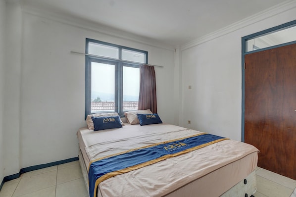 A hotel room with a bed, two windows, a curtain, and a wooden door. - Villa Tjokro 7 By ARBA (Cisarua)