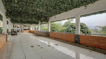 Un espacio interior amplio con suelo de baldosas, un largo banco a lo largo de la pared y vistas a zonas verdes.
