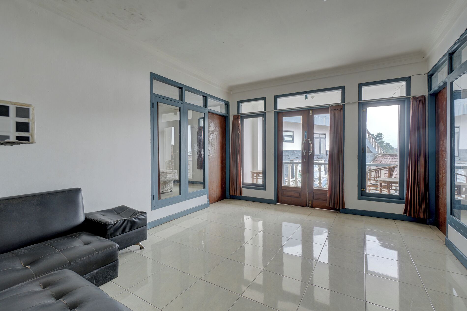 A spacious room with a large window, a black sofa, and a tiled floor.