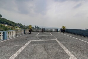 Una zona pavimentada con barandilla, dos plantas en macetas y vista al mar.