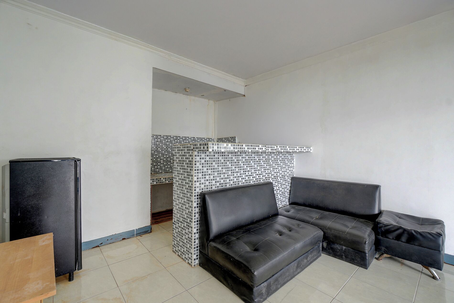 A room with a black refrigerator, a black sofa, and a tiled fireplace.