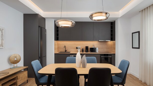 A modern dining area with a wooden table, blue chairs, and a kitchen in the background. - Acropolis Executive Residence  | Chatzichristou Str.16.Athens 11742, Bill & John Apartments & Villas (Athens)