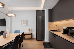 Eine moderne Küche mit integriertem Geschirrspüler, einem schwarzen Kühlschrank und einem Holzes Esstisch mit Stühlen.