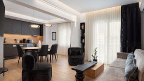A modern living room with a dining area, a kitchen, and a large window with sheer curtains. - Acropolis Executive Residence  | Chatzichristou Str.16.Athens 11742, Bill & John Apartments & Villas (Athens)