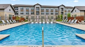 A swimming pool with lounge chairs and umbrellas, surrounded by a building with multiple windows and balconies.