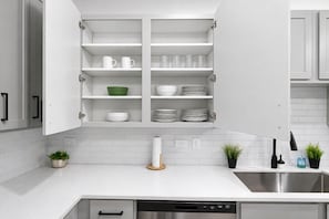 Una cocina moderna con armarios blancos, un lavamanos de acero inoxidable y un escurreplatos.