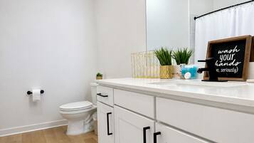 Un baño moderno con un inodoro blanco, un lavabo con espejo y un cartel en el mostrador.