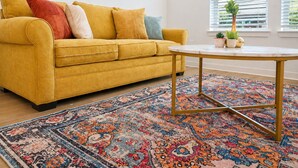 A yellow sofa with multiple cushions, a round table with a gold frame, and a patterned rug.